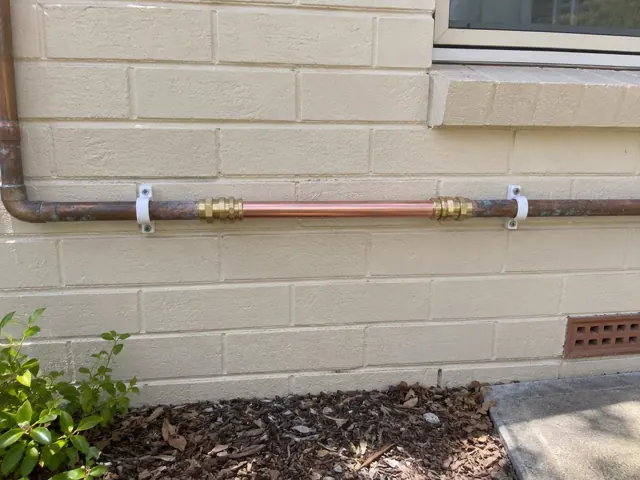 Repaired copper water pipe on a brick exterior wall below a window in Swansea